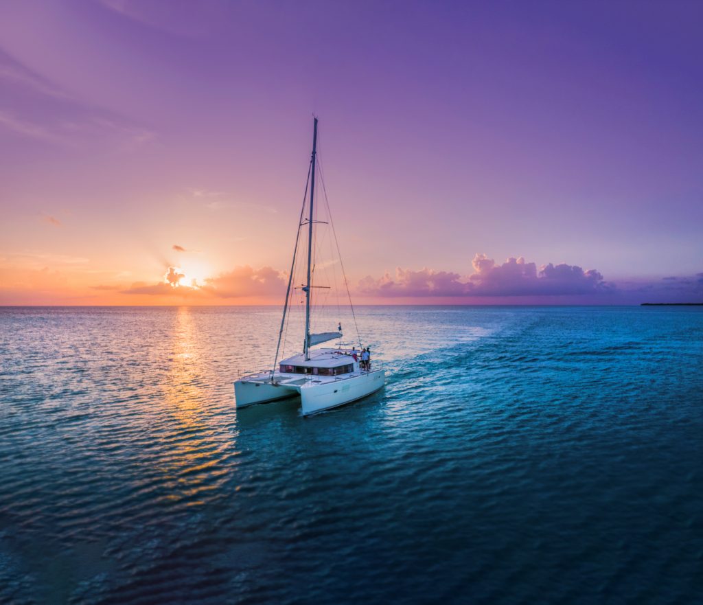 Sailing catamaran heading into a pink and orange sunset