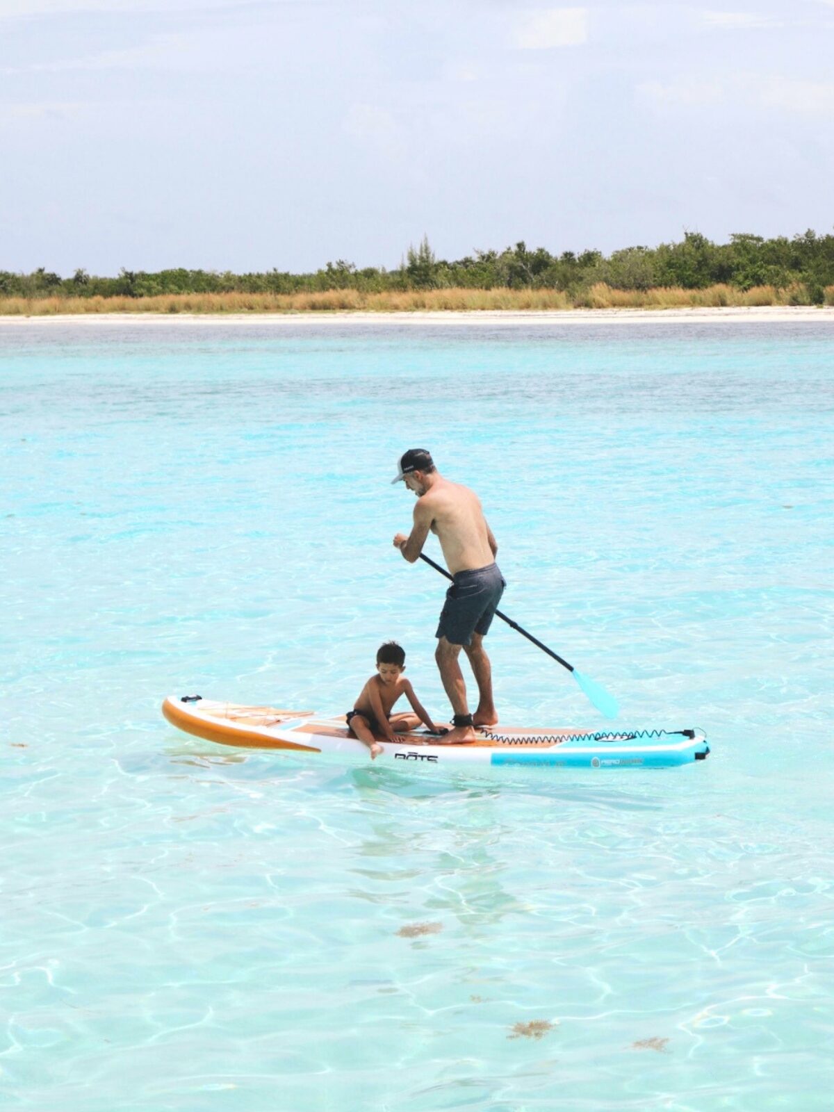 Father and son paddle boarding in the clear shallow water of El Cielo